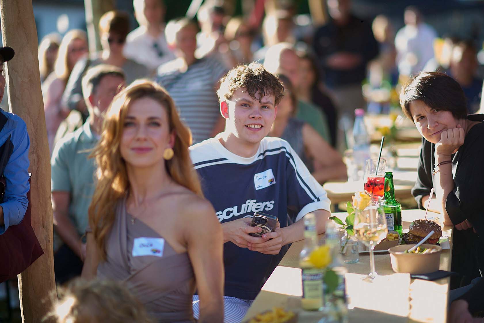 Timon, der duale Student der Agentur sitzt zwischen den Gästen auf einer Bank bei der Jubiläumsfeier